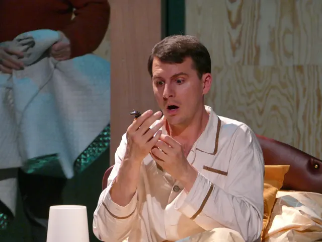 Lukas Eder as the neurasthenic in white pyjamas, with raised hands and a surprised expression.